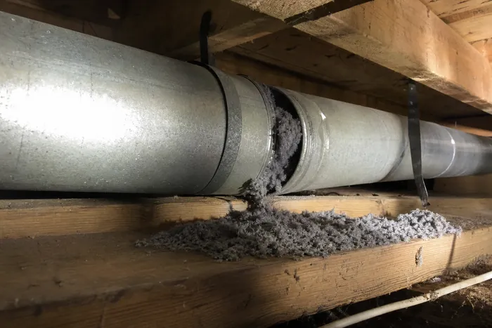 Rigid metal dryer ductwork strapped to floor joists with a joint pulled apart