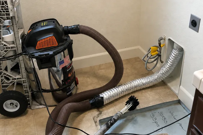 Steve's extraction rig mid-job: hoses run to the wall outlet and a pan of removed lint sits on the laundry-room floor