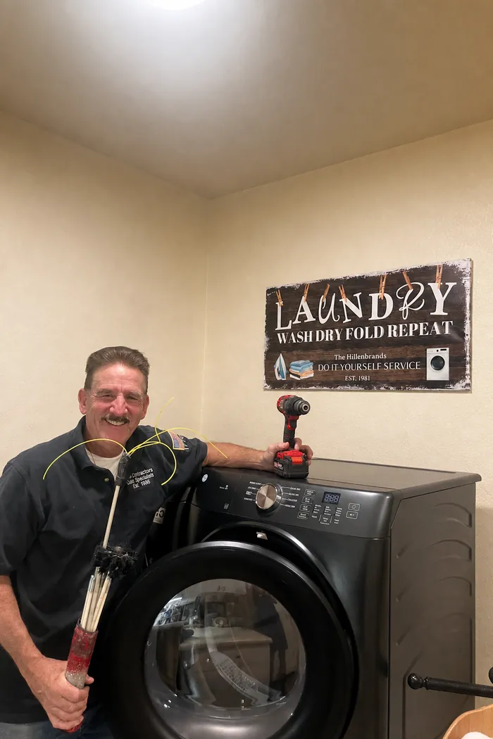 Steve Hillenbrand smiling in a customer's laundry room, holding his cleaning rods and brush